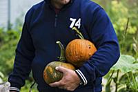 A man holding two squash in the garden